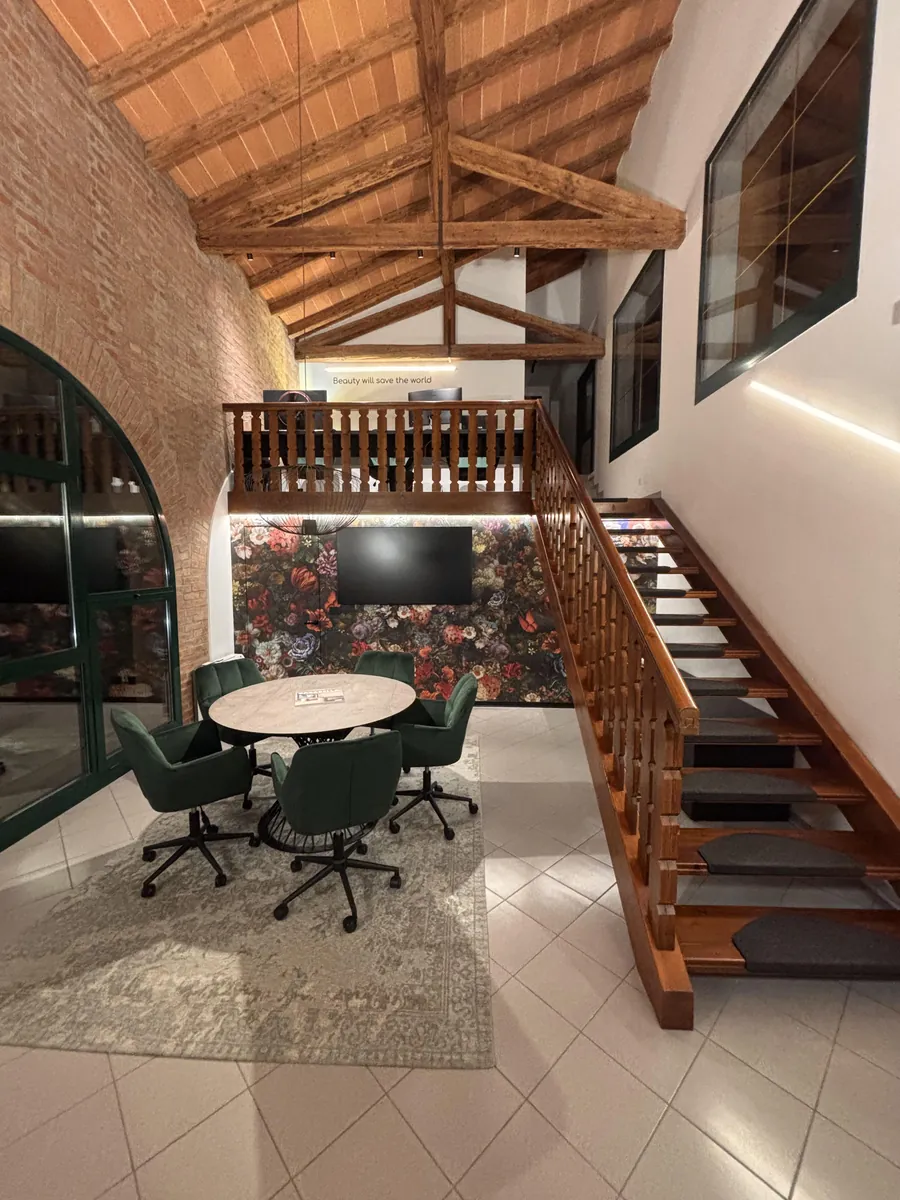 Lo studio FAinteriors a San Stino di Livenza: sala riunioni con travi a vista, scala in legno e sedute verdi
